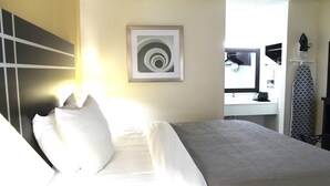 A hotel room with a bed, a framed picture on the wall, a bathroom visible through an open door, and an ironing board.