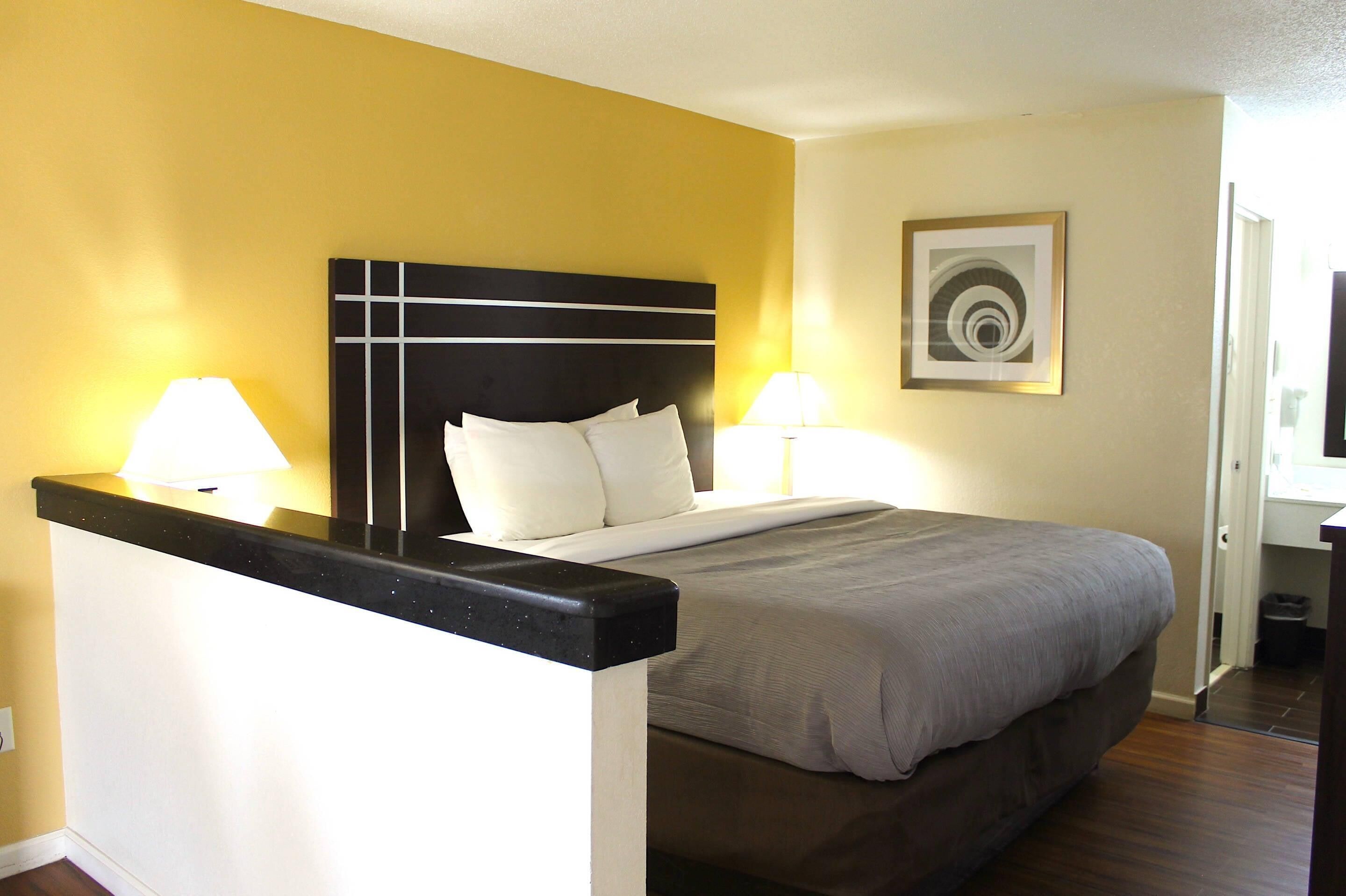 Habitación de hotel con cama, dos lámparas de noche, cabecera y un cuadro en la pared.