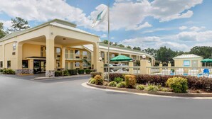A hotel with a covered entrance, a flag, and a pool area with umbrellas.