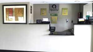A hotel reception desk with a framed artwork, a 'Quality by Choice Hotels' sign, a 'Choice' loyalty card, a digital kiosk, and a telephone.