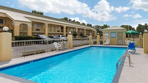 A swimming pool with a poolside area, a covered seating area, and a building with multiple balconies and windows.