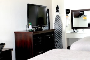 Habitación de hotel con televisión sobre un aparador de madera, espejo sobre el lavabo y cama con colcha gris.