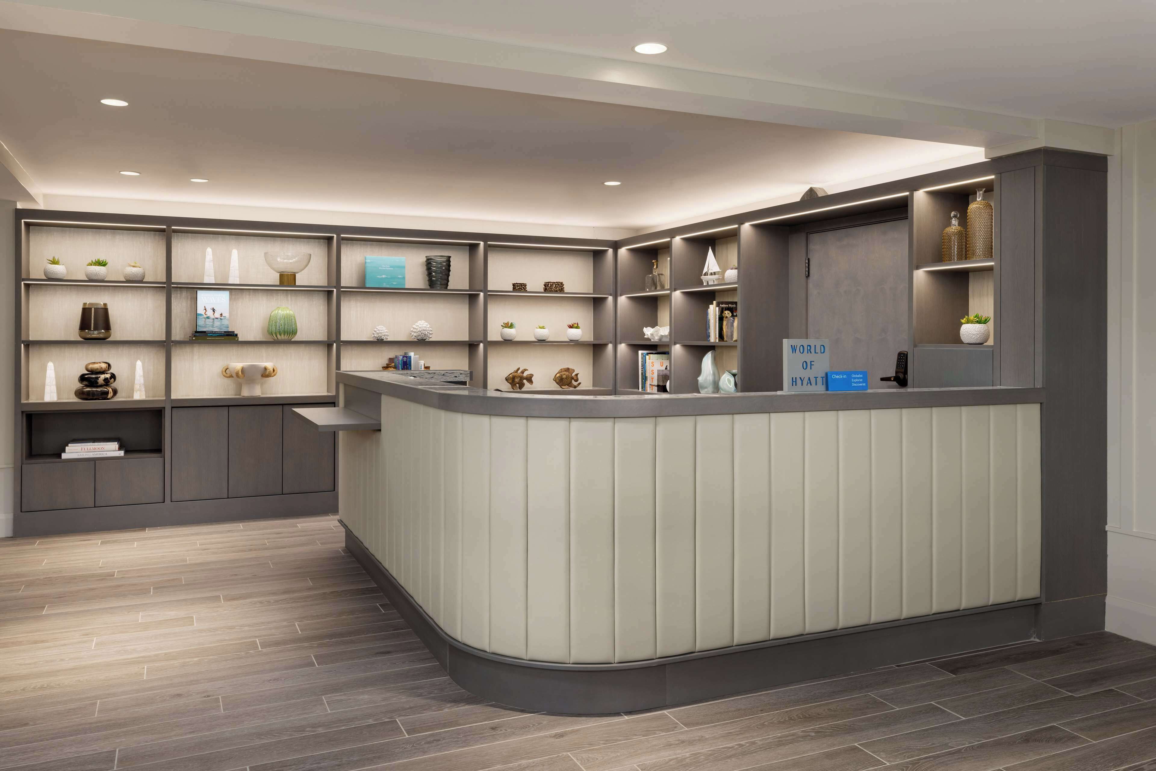 Un área de recepción con un mostrador curvo, estantes con objetos decorativos y un cartel que dice "WORLD OF HYATT".
