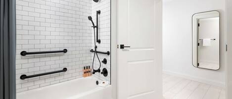 Un baño moderno con una bañera blanca, zona de ducha con mampara de vidrio y un espejo grande en la pared.