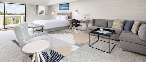A modern hotel room with a large bed, a sofa, a desk, and a view of the outdoors.