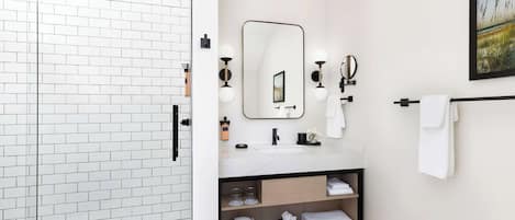 A modern bathroom with a white tiled shower area, a marble sink, and a wooden vanity with shelves for towels.