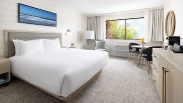 Habitación de hotel con una cama grande, un escritorio con silla, una mesita con un florero, una lámpara y una ventana con cortinas.