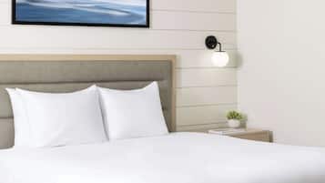 A neatly made bed with white linens, a headboard, and a bedside table with a small plant.