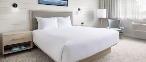 A hotel room with a large bed, a nightstand, a chair, a lamp, and a window with curtains.