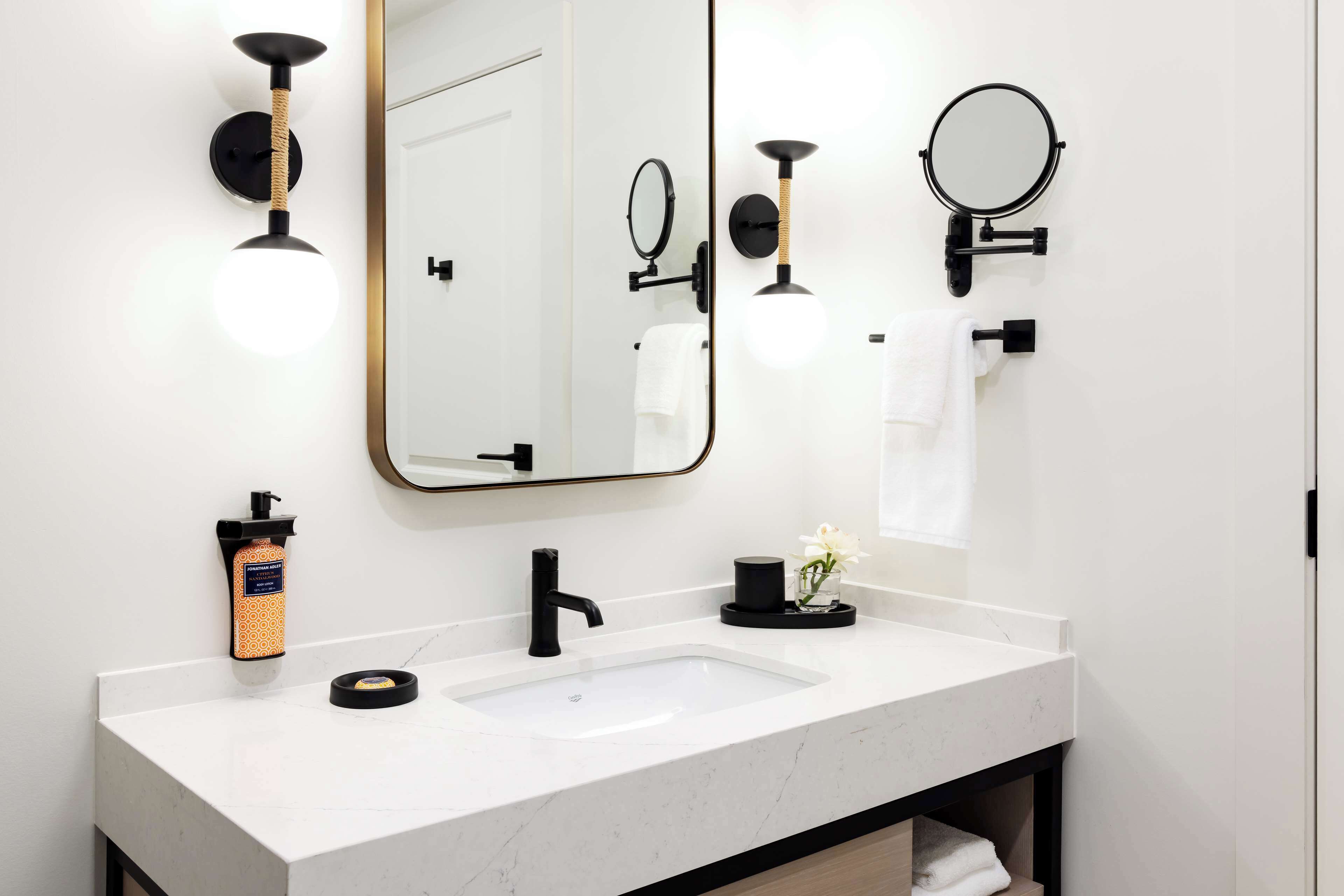 A modern bathroom with a white marble sink, black fixtures, and a large mirror.