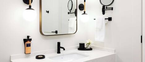 A modern bathroom with a white marble sink, black fixtures, and a large mirror.