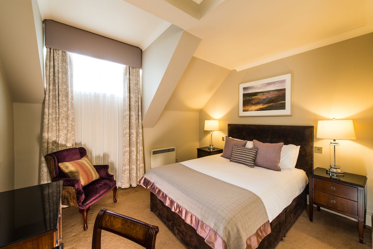 A hotel room with a large bed, two bedside tables, a chair, a desk, and a painting on the wall.