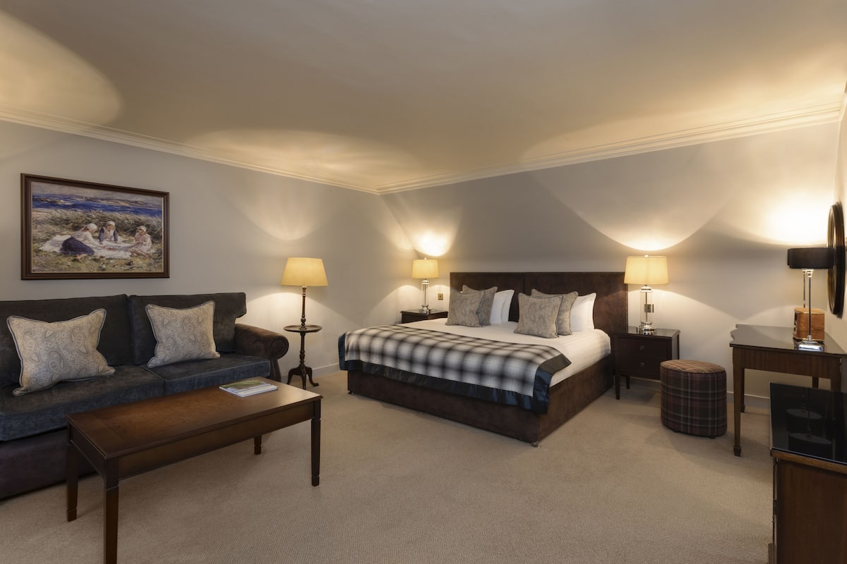 A hotel room with a large bed, a sofa, a coffee table, and two bedside lamps.