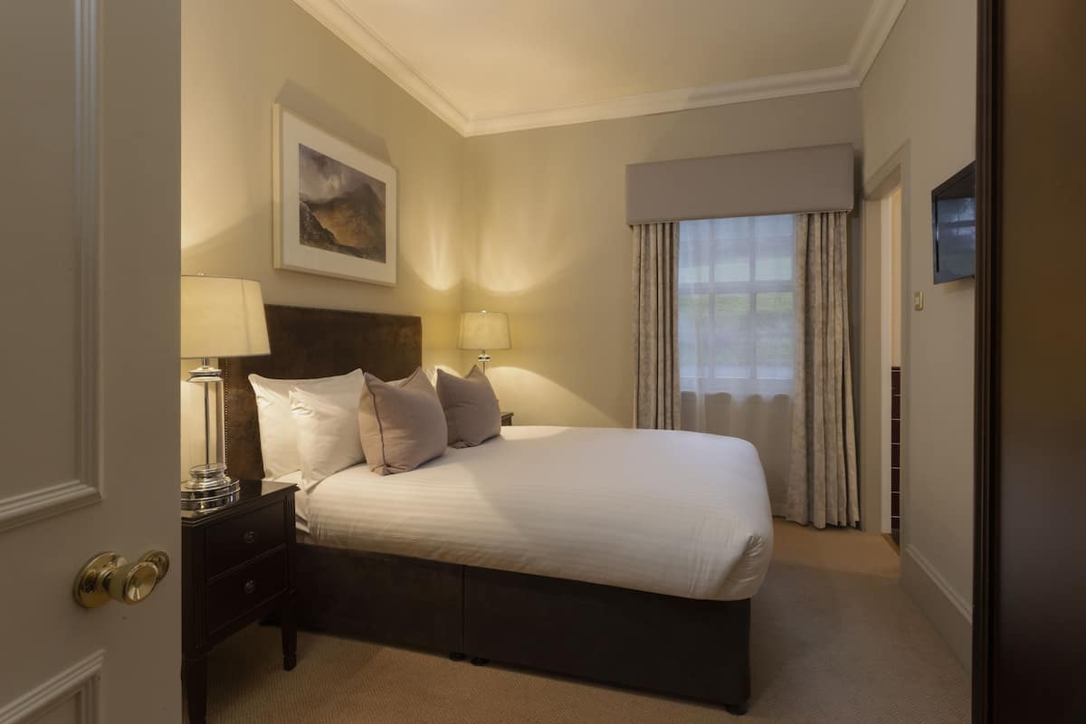 A hotel room with a large bed, two bedside tables with lamps, a painting on the wall, and a TV on the wall.