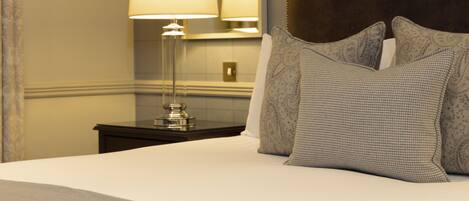 A neatly made bed with patterned pillows, a bedside lamp, and a dark nightstand in a hotel room.