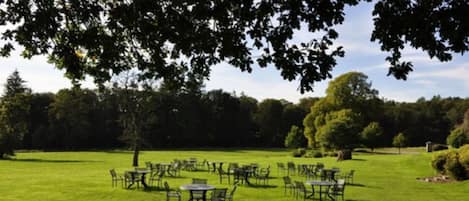 An outdoor seating area with tables and chairs arranged on a grassy field.