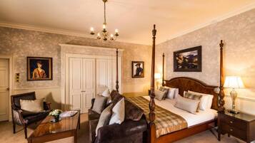 Un lit à baldaquin avec une tête de lit en bois, un coin salon avec un canapé et un fauteuil, une table basse en bois avec un vase, et une table de chevet avec une lampe.