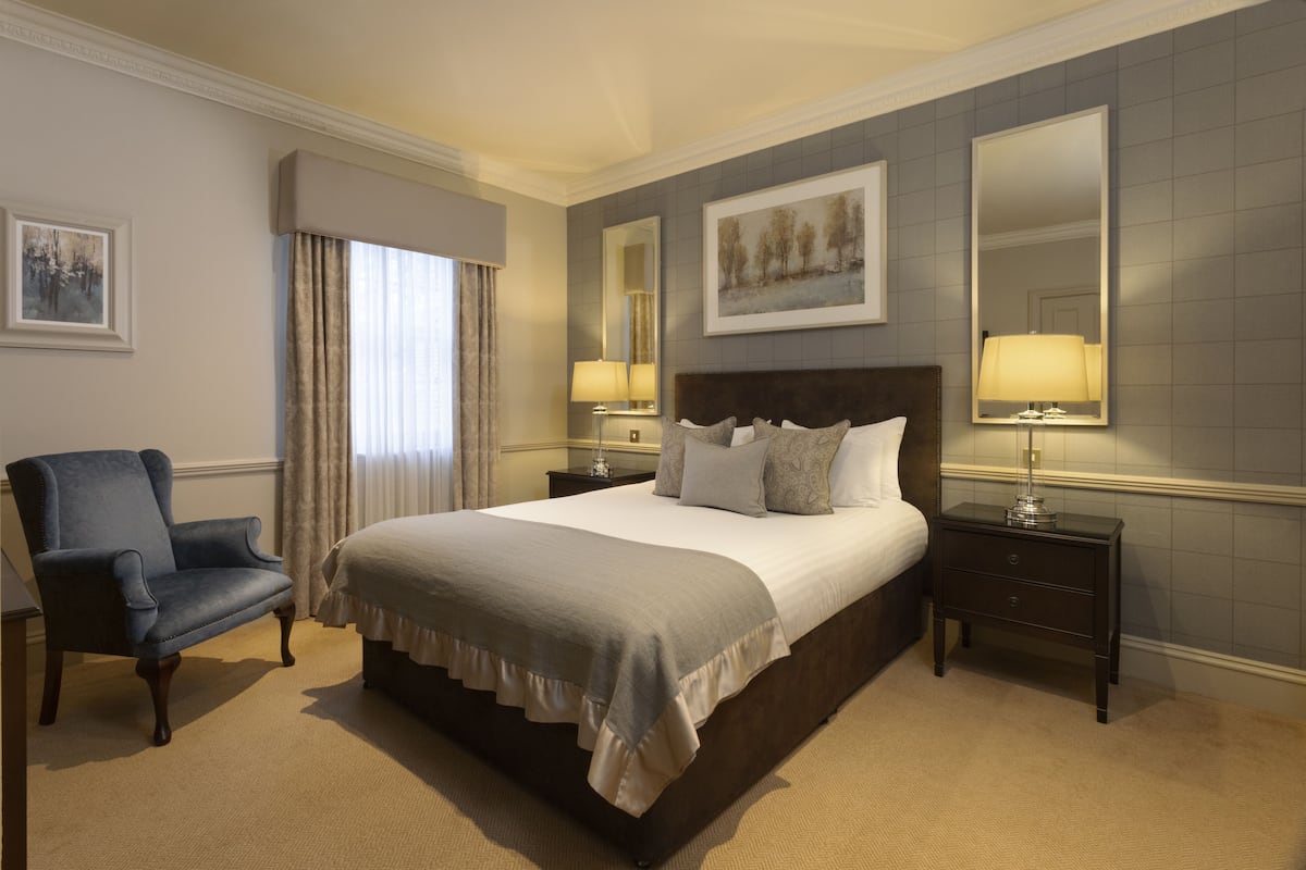 A neatly arranged hotel room with a large bed, a chair, two bedside tables with lamps, and a large mirror on the wall.