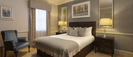 A neatly arranged hotel room with a large bed, a chair, two bedside tables with lamps, and a large mirror on the wall.