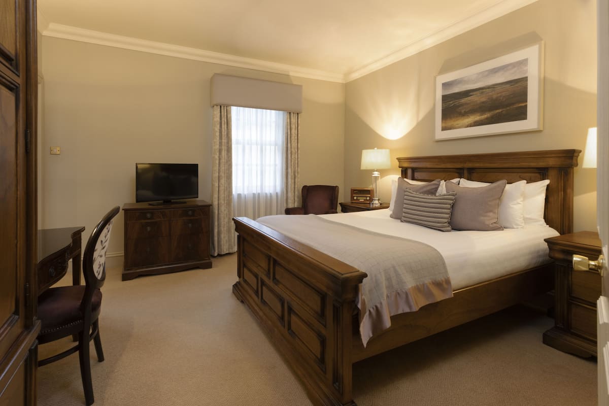 A hotel room with a large bed, a television, a desk with a chair, and a painting on the wall.