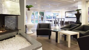 A modern interior with a fireplace, seating area, and large windows. - Novotel Fontainebleau Ury (Ury)