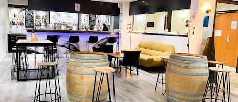 A bar area with wooden barrels, stools, and a sofa.