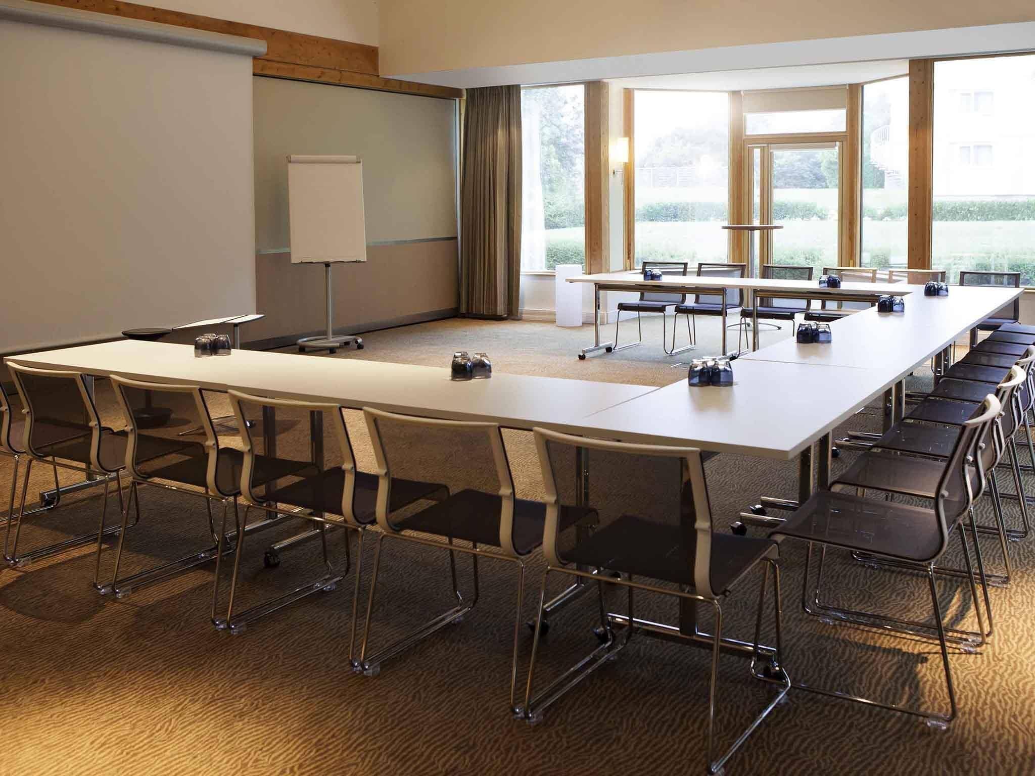 A conference room with a long table, chairs, a projector screen, and large windows.
