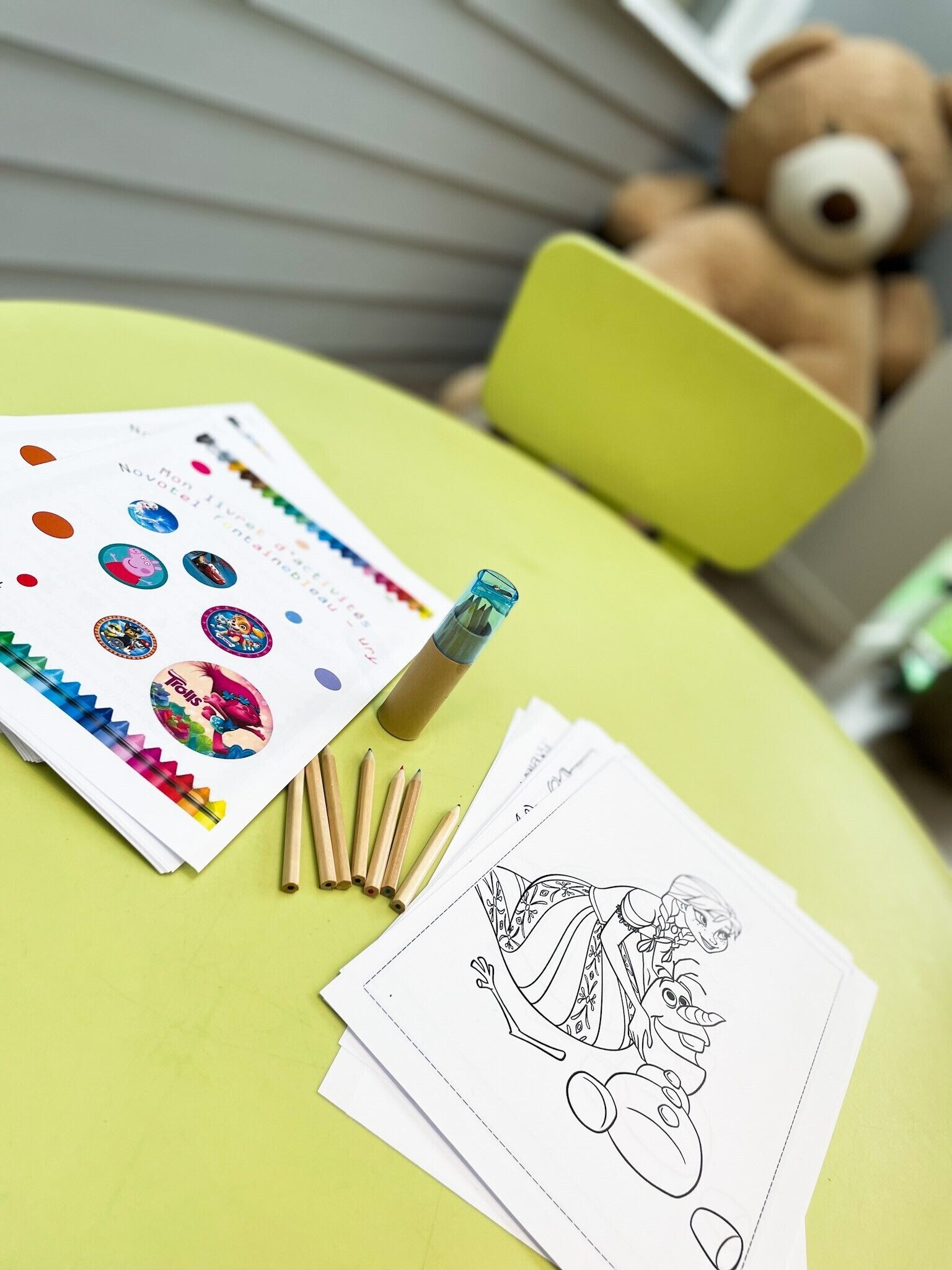 A table with coloring pages, pencils, and a bottle.