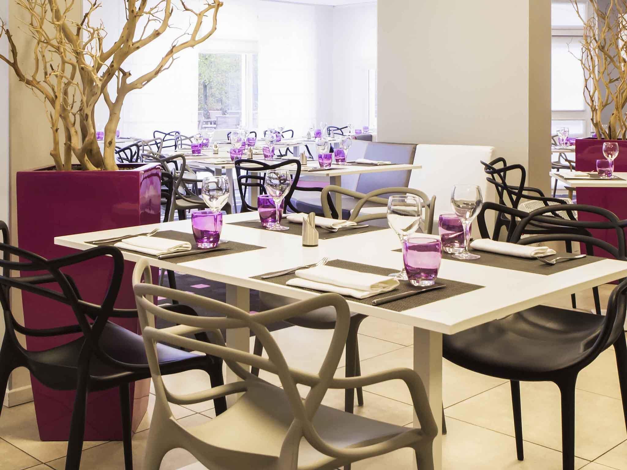 Un espace repas avec des tables dressées pour quatre personnes, chacune agrémentée de verres violets et de serviettes blanches.