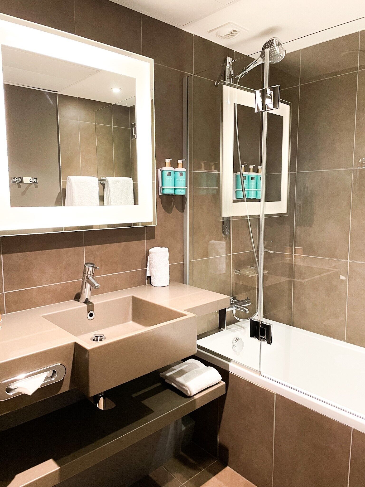 Un baño moderno con un espejo grande, dos lavamanos, una ducha y un perchero para toallas.