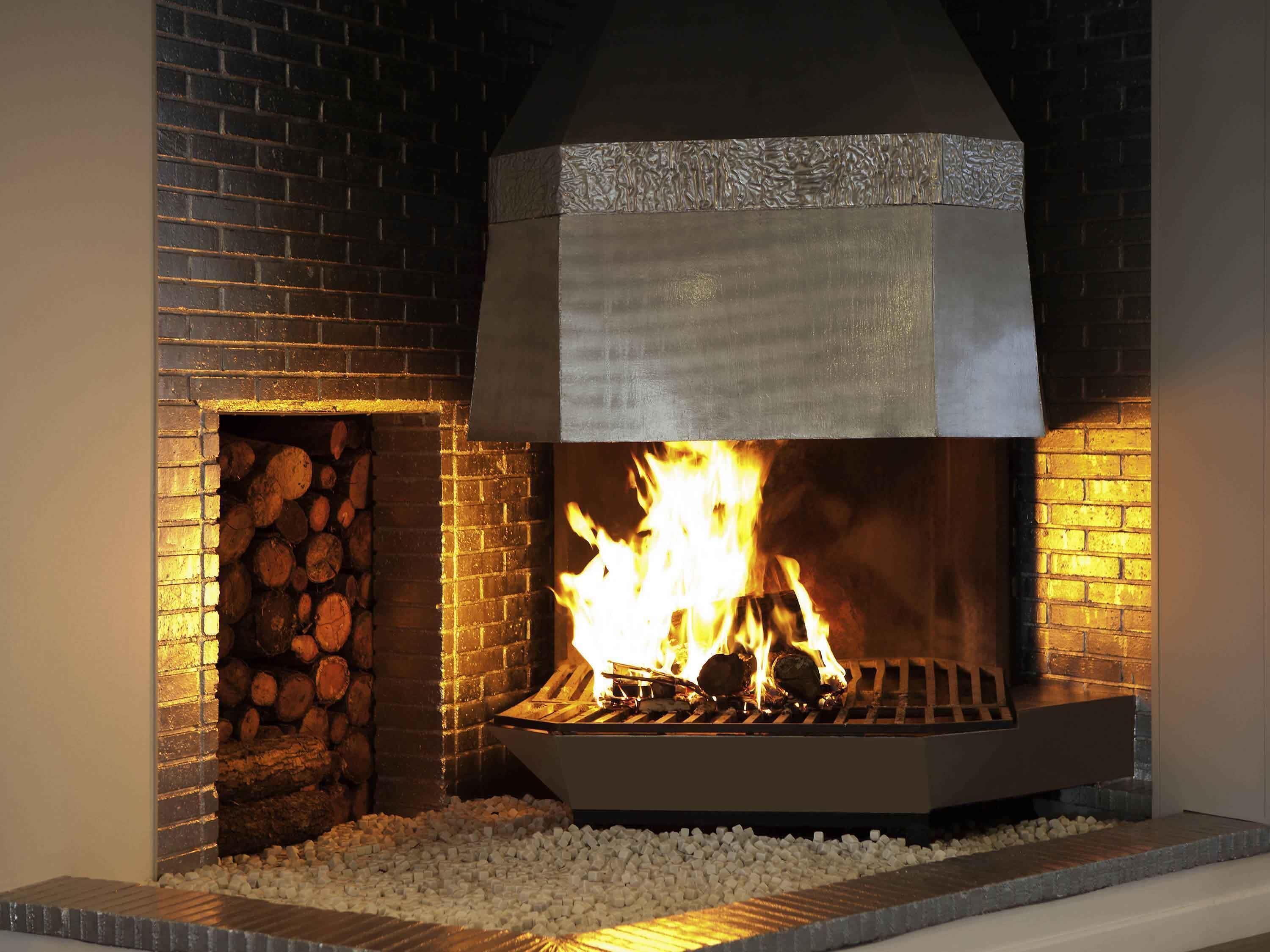 A fireplace with logs, a stone surround, and a metal cover.