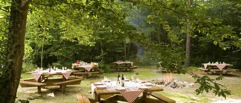 An outdoor dining area with picnic tables set up in a forested setting.