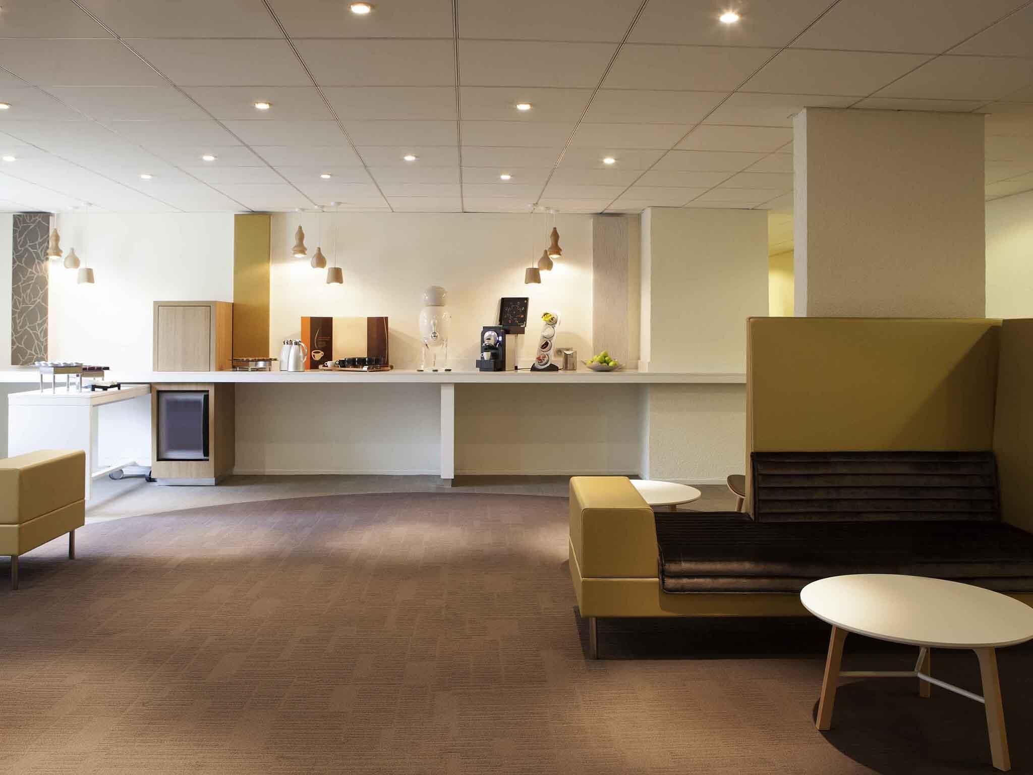Un hall d’hôtel moderne avec un comptoir d’accueil, un espace salon et une machine à café.