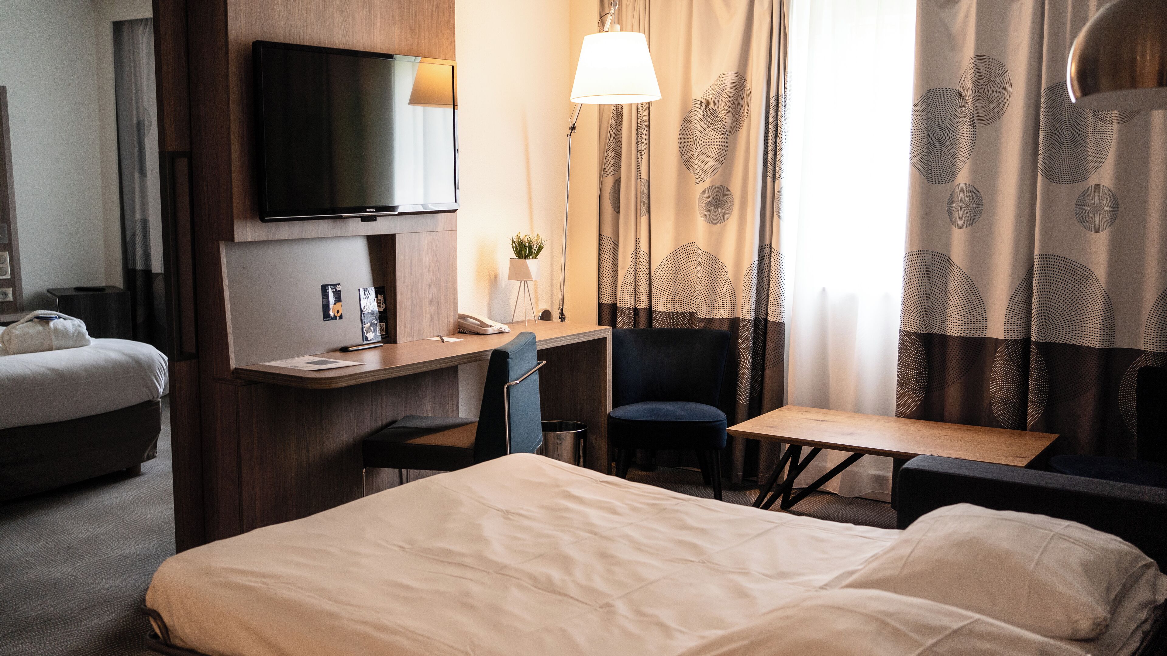 Une chambre d’hôtel équipée d’un lit, d’un bureau, d’une chaise, d’une télévision et de rideaux.