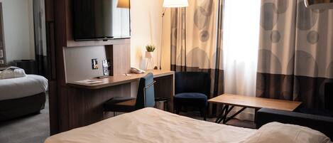 A hotel room with a bed, a desk, a chair, a television, and curtains.