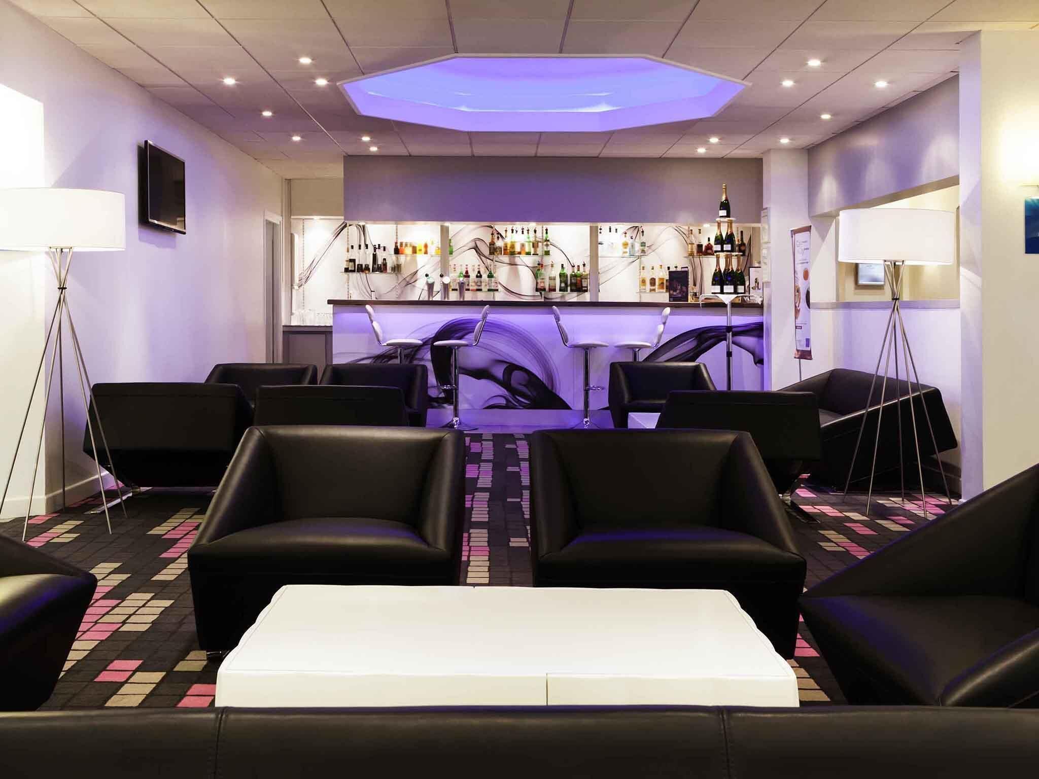 A bar area with a counter, bar stools, and a seating area with chairs and a white table.