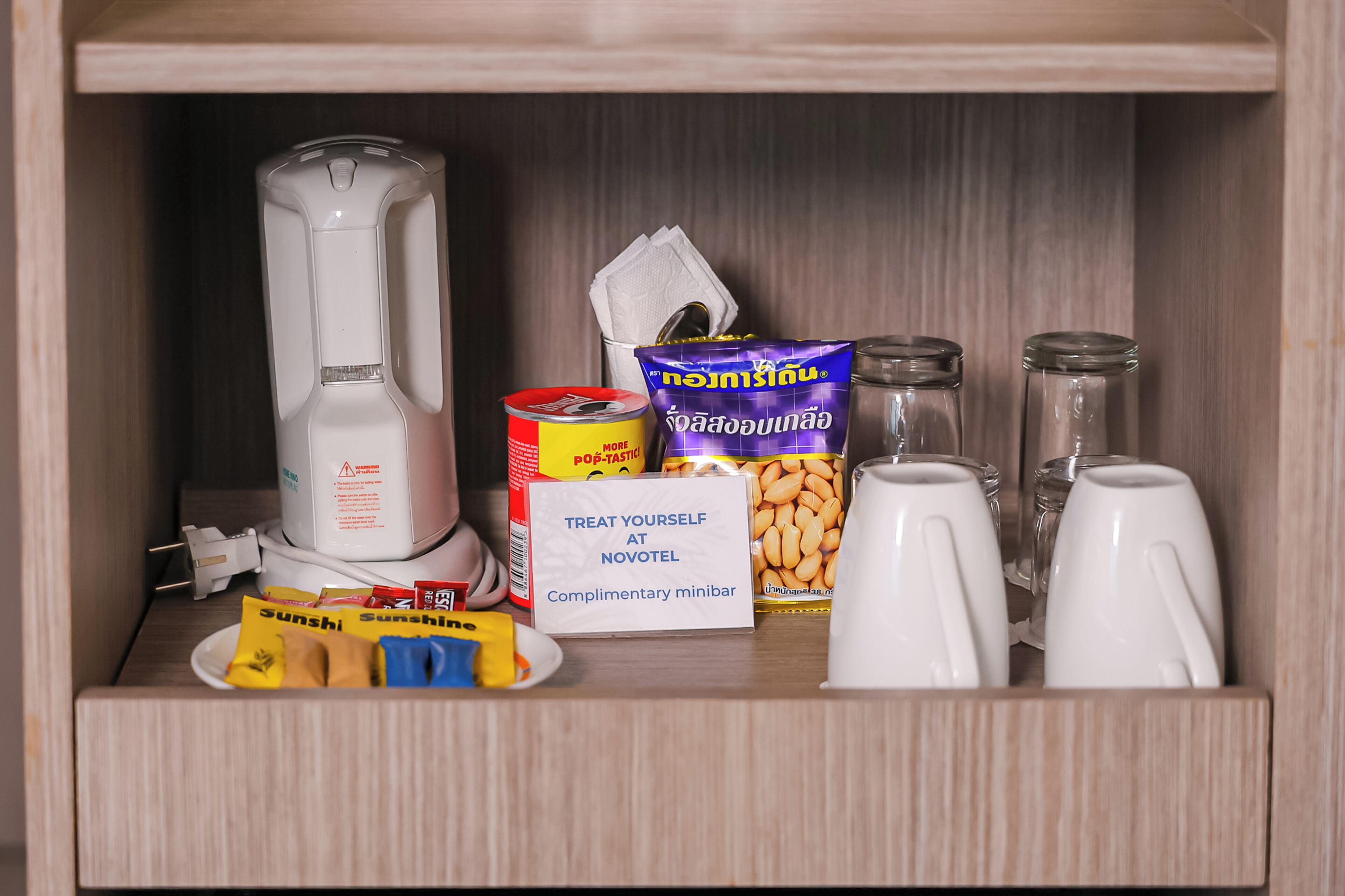 A minibar with a coffee maker, snacks, a can of pop, a packet of nuts, and salt and pepper shakers.