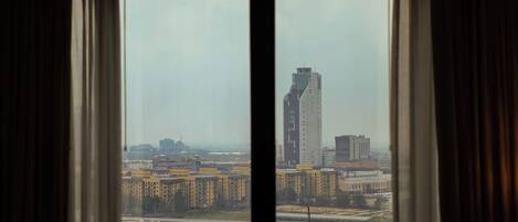 A view through a window with curtains, featuring a cityscape with buildings and a bridge.