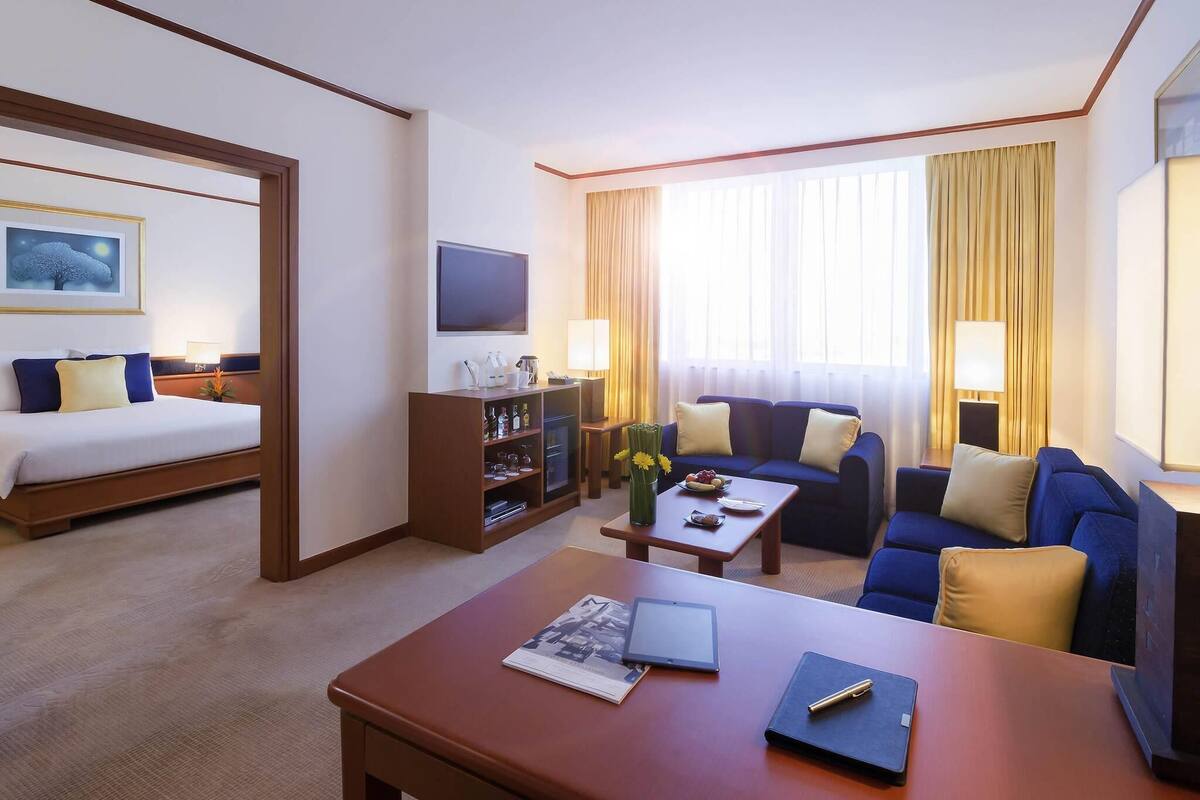 A hotel room with a bed, a sofa, a coffee table, a TV, and a minibar.