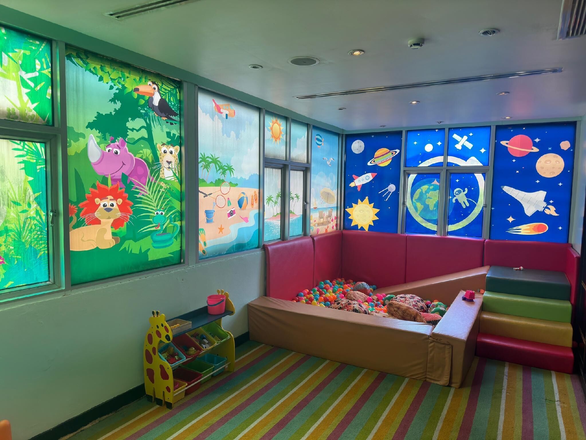 A children's playroom with colorful murals, a play area with a ball pit, and a seating area with a bench.