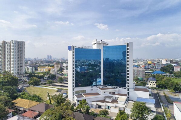 Un hôtel moderne à la façade en verre, entouré d’autres immeubles et de verdure.