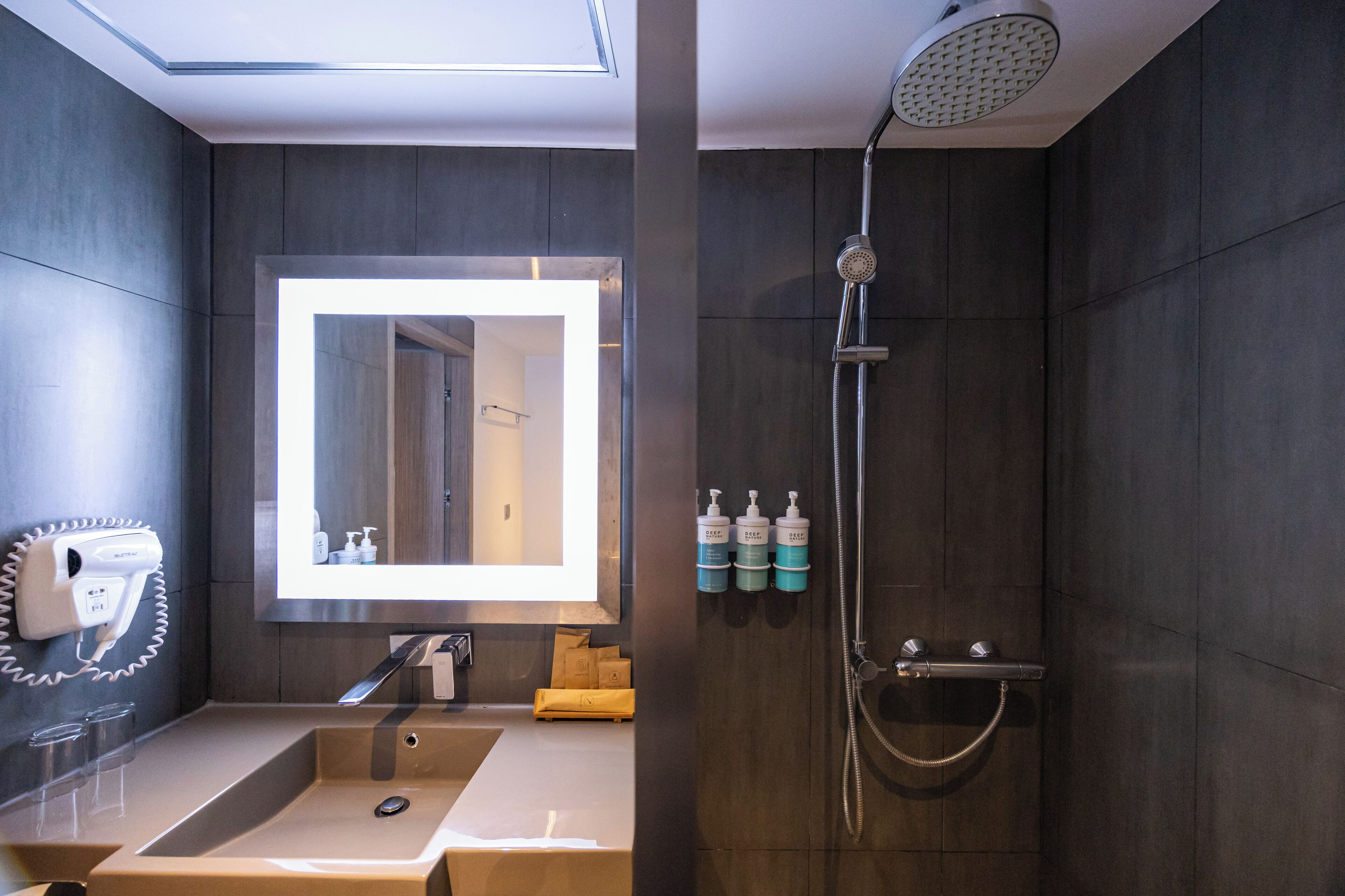 Un baño moderno con un espejo grande, un cabezal de ducha de mano y un lavabo con toallero.