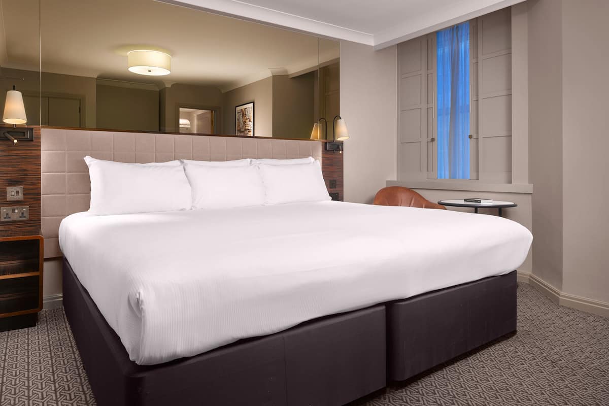 Ett modernt hotellrum med en stor säng, ett litet bord och en garderob.