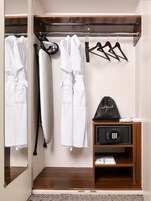 Um banheiro de hotel com espelho, um porta-toalhas com toalhas brancas, um secador de cabelo e uma bolsa preta com a etiqueta "HAIR DRYER" sobre uma prateleira de madeira.