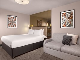 Ein Hotelzimmer mit einem großen Bett, einem grauen Sofa und zwei gerahmten Kunstwerken an den Wänden.