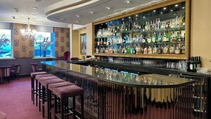 A bar area with a mirrored wall, multiple liquor bottles, and bar stools. - Strand Palace Hotel (London)
