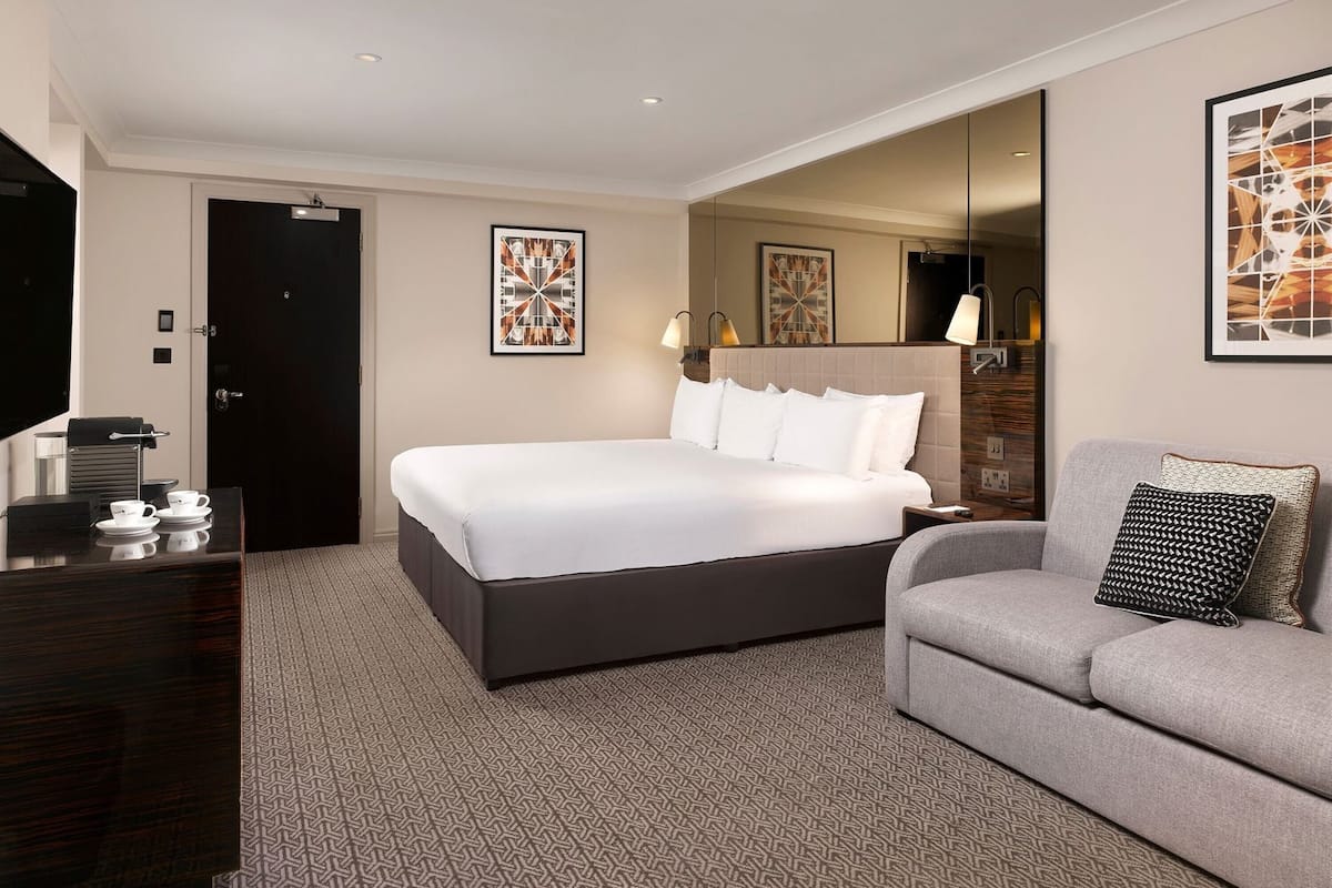 Ett hotellrum med en stor säng, en soffa, en tv och konstverk på väggarna.