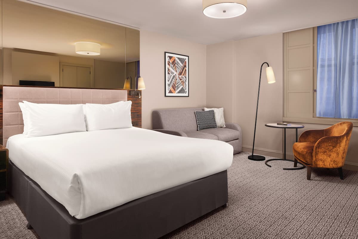 Ett hotellrum med en stor säng, en soffa, ett litet bord och en stol.