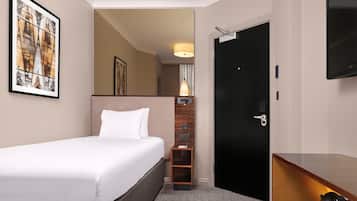 A hotel room with a bed, a desk with a coffee maker, a TV, and a door.