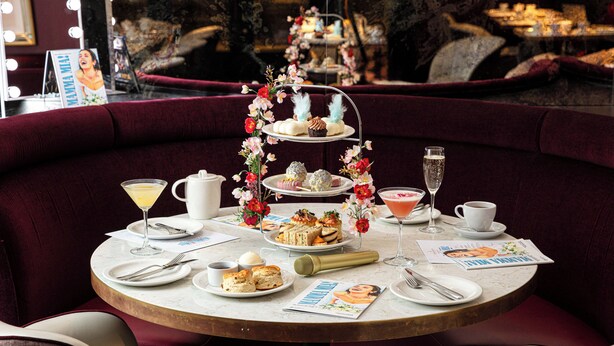 A round table with a tiered dessert stand, plates of food, and a magazine. - Strand Palace Hotel (London)
